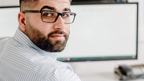 Der junge Mann trägt ein gestreiftes Hemd und wirkt konzentriert, während er an seinem Arbeitsplatz arbeitet.