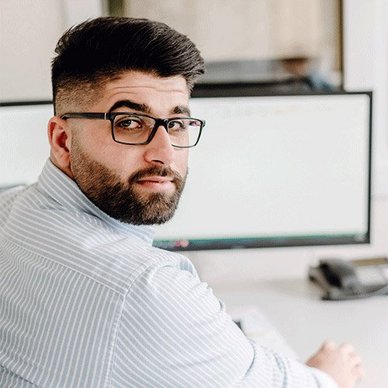 Der junge Mann trägt ein gestreiftes Hemd und wirkt konzentriert, während er an seinem Arbeitsplatz arbeitet.