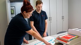 Zwei Mitarbeiter von Büürma betrachten gemeinsam technische Zeichnungen auf einem Tisch im Büro