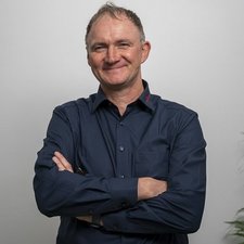 Der Mann trägt ein dunkelblaues Hemd und strahlt Selbstbewusstsein und Zufriedenheit aus.