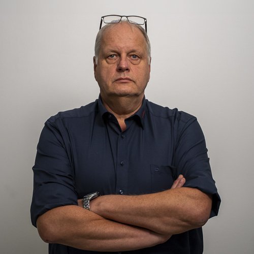 Der Mann trägt ein dunkelblaues Hemd und hat eine Brille auf dem Kopf, während er direkt in die Kamera schaut.