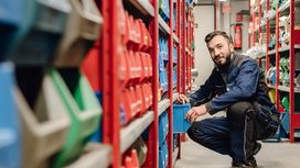 In einem gut organisierten Lagerraum sortiert ein Arbeiter blaue Kisten und zeigt dabei ein freundliches Lächeln.