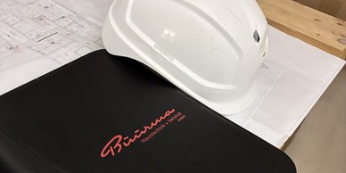 Weißer Schutzhelm liegt auf Unterlagen und einer Mappe mit Büürma Logo
