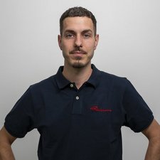 Porträt eines Mannes mit neutralem Gesichtsausdruck Der junge Mann mit einem selbstbewussten Ausdruck hat ein Polohemd mit rotem Schriftzug und posiert in einem minimalistischen Raum.