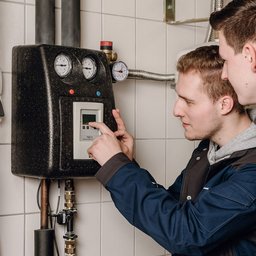 In einem modernen Technikraum arbeiten zwei Männer an einem Bedienfeld, um Einstellungen vorzunehmen und Informationen abzulesen.