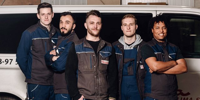 Die Gruppe von fünf Männern in blauen Overalls posiert selbstbewusst vor einem weißen Lieferwagen, bereit für die Arbeit.