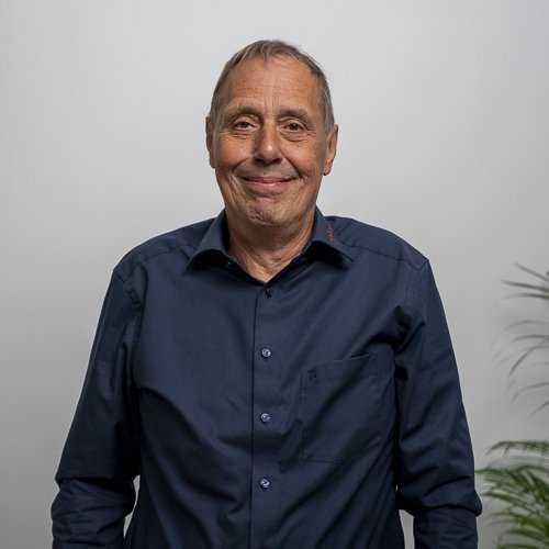 Der Mann in der Mitte des Bildes hat graue Haare und strahlt eine positive Ausstrahlung aus, umgeben von einer Pflanze.