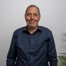 Portrait eines freundlichen älteren Herren mit natürlichem Lächeln Der Mann in der Mitte des Bildes hat graue Haare und strahlt eine positive Ausstrahlung aus, umgeben von einer Pflanze.