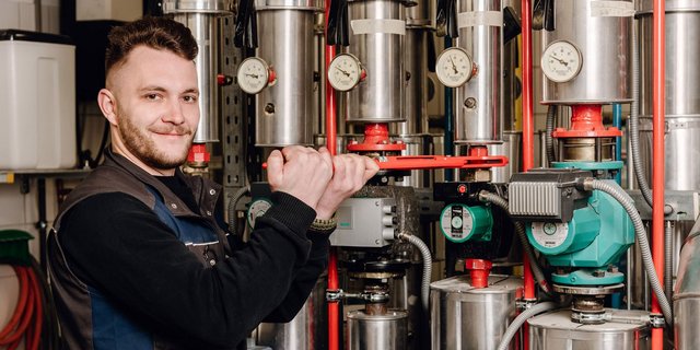 Der Techniker greift mit beiden Händen ein rotes Werkzeug, um eine Maschine in einer industriellen Umgebung zu reparieren.