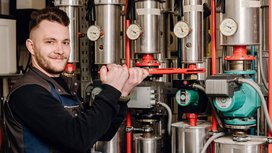 Der Techniker greift mit beiden Händen ein rotes Werkzeug, um eine Maschine in einer industriellen Umgebung zu reparieren.