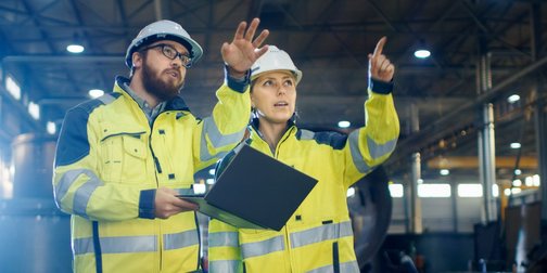 Ein Mann und eine Frau die einen Bauhelm und eine Warnjacke tragen 