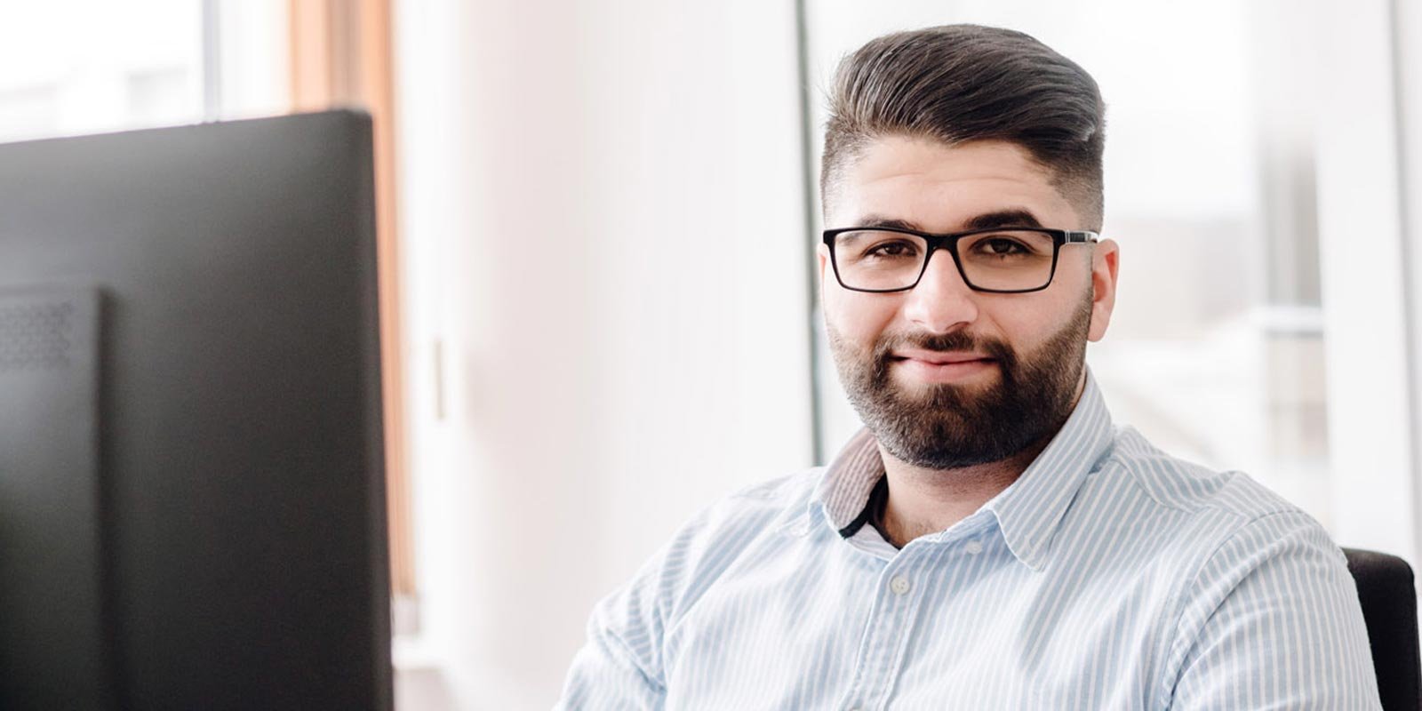 In einem hellen Raum sitzt ein Mann mit Bart und Brille, der entspannt in die Kamera lächelt.